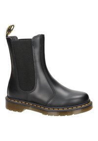 Bota de tobillo de cuero negro con paneles laterales elásticos, costuras amarillas, asa en la parte superior y suela de goma translúcida.
