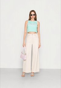 Top cropped em verde menta com bainha escavada, calças largas bejes, bolsa rosa clara, e chinelos aqua. Óculos de sol pretos usados.