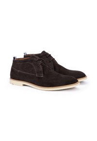 Bottines chukka en daim marron avec une semelle en caoutchouc, dotées d'un bout arrondi, de coutures minimales et d'une accentuation bleue à l'arrière.