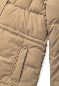 Beżowa kurtka puchowa o pikowanym wzorze, z boczną kieszenią i gładką fakturą. Materiał wydaje się lekki, ale jednocześnie dobrze ocieplony.