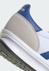 Baskets basses avec une tige en mesh blanc, des accents en cuir bleu, un talon en suède gris et une semelle extérieure en caoutchouc noir texturé. Marquage "CLOUDFOAM" visible.