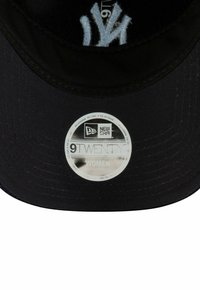 Casquette réglable New Era 9TWENTY noire pour femmes avec une visière incurvée, arborant un logo brodé blanc et une étiquette réfléchissante. Tissu texturé.