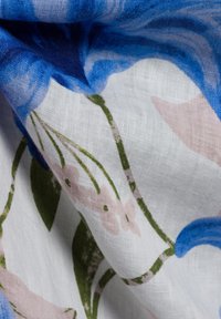 Blumenstoff mit blauen und rosa Blumen auf einem weißen Hintergrund, mit grünen Blättern, strukturierter Leinenwebung und leicht zerknitterter Oberfläche.