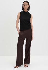 Top nero senza maniche con collo alto, abbinato a pantaloni larghi marroni scuri. Tessuto liscio, design minimale, senza motivi o parti metalliche visibili.