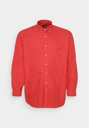 Chemise rouge à boutons, en coton, avec un col évasé, des manches longues et un petit logo bleu sur la poitrine gauche. Texture lisse.