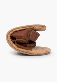 Brązowe skórzane sandaly z korkową wkładką, z miękkimi detalami i regulowanymi paskami, pokazane w złożonej pozycji. Miękka tekstura i zaokrąglony kształt.