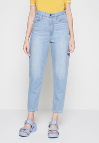 Jeans de talle alto en azul claro con corte recto, que cuentan con bolsillos frontales y una sutil textura desgastada, combinados con sandalias de plataforma en azul claro.