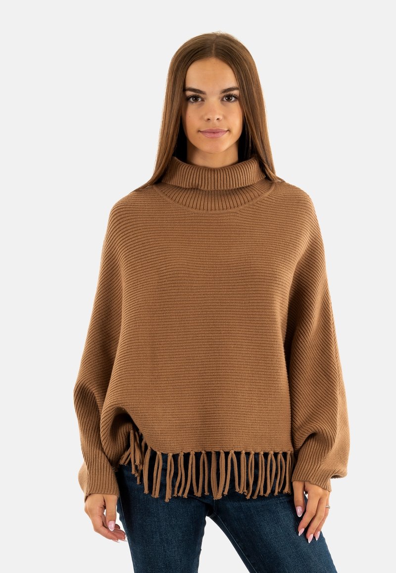 Pull en tricot marron avec un col roulé haut, des franges au niveau de l'ourlet, et une coupe ample, associé à un jean bleu foncé.