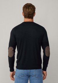 Czarny sweter z długimi rękawami i okrągłym dekoltem, z beżowymi łatek na łokciach. Tkanina wydaje się gładka i dopasowana.