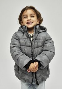 Graue Pufferjacke mit Dinosauriermustern, Kapuze und schwarzen Bündchen. Reißverschluss vorne und gestepptes Material, getragen von einem Kind.
