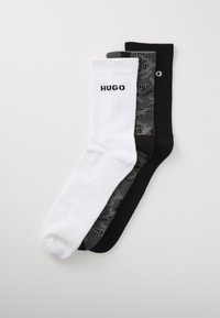 Trois paires de chaussettes de sport en blanc, camouflage gris et noir, chacune avec le texte "HUGO" sur le poignet, disposées à plat sur un fond blanc.