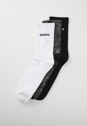 Drei Paar Crew-Socken in Weiß, grau camouflierte und schwarzer Farbe, jeweils mit dem Text "HUGO" am Bündchen, flach auf einem weißen Hintergrund angeordnet.