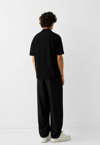 Top nera a maniche corte con un motivo texturizzato, abbinata a pantaloni neri larghi e sneaker chiare. Design minimalista.