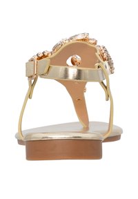 Sandales dorées avec une semelle plate, présentant une bande décorative de strass transparents sur le dessus et une fine bride à la cheville.