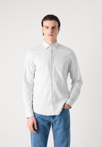 Weißes Langarmhemd mit feinem vertikalem Streifenmuster, Button-Down-Kragen und normaler Passform, kombiniert mit hellblauen Jeans.