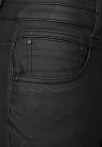 Jeans negros con un diseño clásico de cinco bolsillos, textura suave, costuras en contraste y acentos metálicos en el bolsillo trasero.