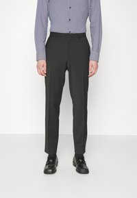 Pantaloni neri su misura con una vestibilità slim, dotati di tasche laterali e una texture morbida. Abbinati a una camicia a maniche lunghe con fantasia e mocassini neri.