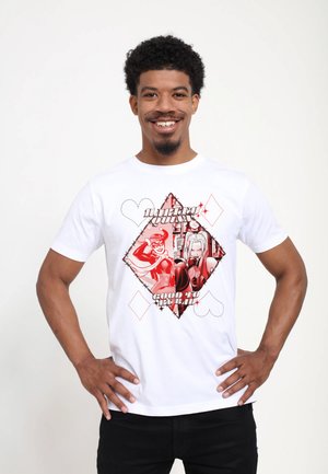 Lachende man met een wit T-shirt met een rood diamantvormig grafisch ontwerp met twee vrouwelijke superhelden en de tekst "Quinn Good to be Bad."
