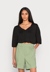 Top preto cropped com decote em V e mangas curtas bufantes, combinado com calções verde-claro de cintura alta com uma faixa elástica.