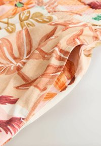 Tela con estampado floral en tonos melocotón, naranja y verde, con una textura suave y bordes cosidos, mostrando una sección doblada.