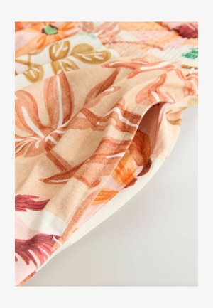 Kankaan, jossa on kukkakuosi persikan, oranssin ja vihreän sävyissä, sileä pinta ja ommellut reunat, esittelee taitettua osaa.