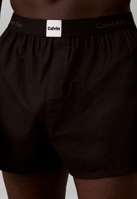 Czarne bawełniane bokserki z elastycznym paskiem w talii z białym logo "Calvin Klein". Gładka tekstura i luźny krój.