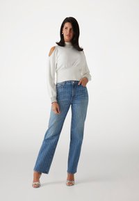 Pulover alb cu umeri descoperiți, cu margine ribbed, asortat cu blugi largi rayé albaștri. Pantofii cu toc argintii completează look-ul.