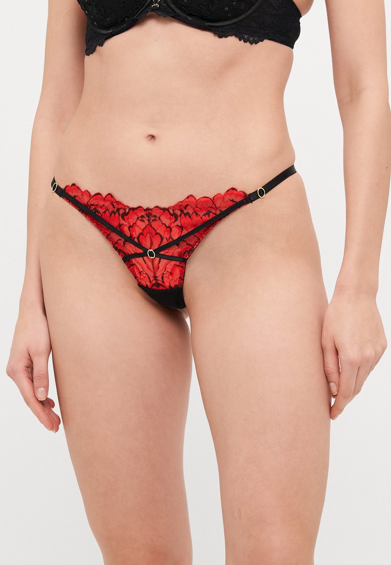 Rød blonde tanga med svart kant, med blomsterdesign, gullfargede detaljer og tynne stropper for et delikat uttrykk.