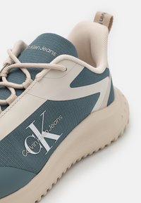 Svetlomodrá a béžová športová obuv s textúrovanou tkaninou, bielymi akcentmi a logom "Calvin Klein Jeans". Obsahuje polstrovanú podrážku a šnúrky.