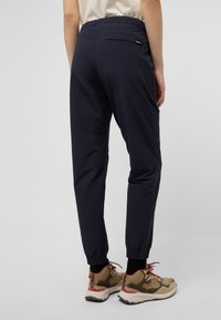 Pantalons de jogging navy avec une taille élastique, des jambes fuselées et des poignets élastiques. Comprend une poche arrière et portés avec des baskets beiges et rouges.