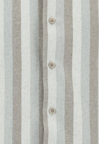 Koszula w paski z guzikami w kolorze jasnoszarym i beżowym, oferująca trzy okrągłe, beżowe guziki oraz teksturowany materiał z naprzemiennymi szerokimi i wąskimi paskami.
