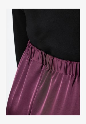 Fioletowa satynowa spódnica z elastycznym pasem, o gładkiej fakturze i delikatnym połysku. Górna część jest czarna i dopasowana.