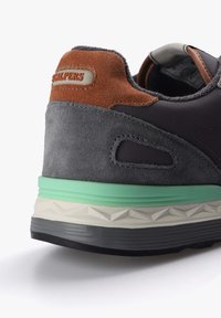 Sneaker din suede gri cu accente maro, talpă neagră și verde. Are un design texturat și o etichetă cu logo pe spate.