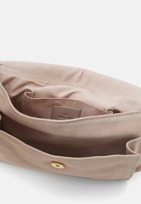 Wnętrze torby z jasnobeżowej tkaniny o gładkiej fakturze, z małą kieszonką i złotym zapięciem na zatrzask. Podszewka jest miękka i nieozdobiona.