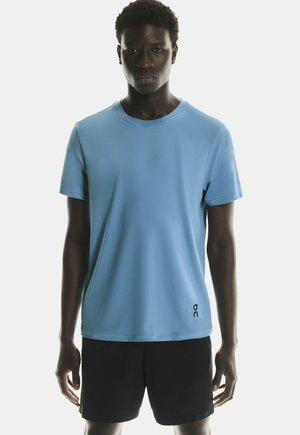 Ljusblå kortärmad T-shirt med rund halsringning och svarta logodetaljer nere till vänster. Kombinerad med svarta shorts.