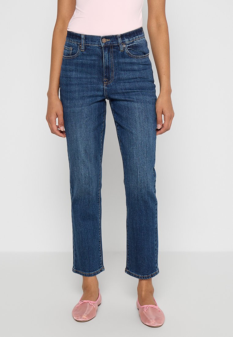 Blaue Jeans mit klassischer Passform, hoher Taille, Fünf-Taschen-Design und leichter Ausbleichung, kombiniert mit rosa Slippers.