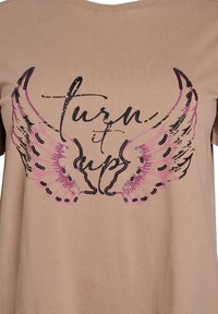 Beige T-Shirt mit schwarzem Text "turn it up" und pinken Flügel-Illustrationen, geprägt von detaillierten Mustern und Akzenten, samtweiche Stofftextur.