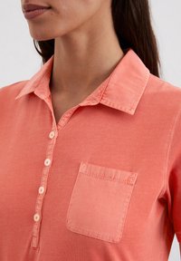 Koraalrode button-up shirt met een kraag, subtiele textuur en een linkse borstzak. Voorzien van vier bijpassende knopen aan de voorkant.