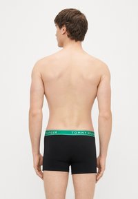 Cuecas boxer pretas com um cós verde com o logótipo "TOMMY HILFIGER". Tecido macio, design ajustado, estilo minimalista.