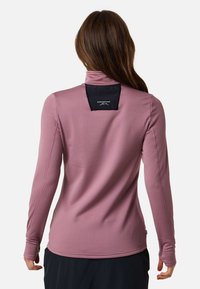 Long-sleeve, form-fitting top in light purple with a textured finish and a stand-up collar. Features a black tag at the back with branding.
