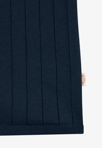 Section de tissu tricoté côtelé bleu foncé avec des lignes verticales et une petite étiquette beige sur le côté droit montrant un texte partiellement visible.