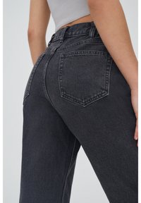 Jean taille haute en denim gris foncé avec cinq poches, surpiqûres contrastées et coupe décontractée. Tissu texturé avec un léger effet stretch.