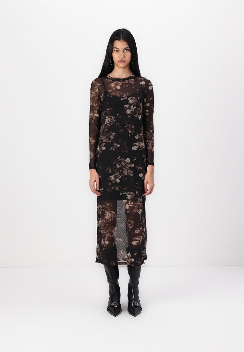 Robe en mesh noire à fleurs avec des manches longues, un corps transparent et une fente jusqu'à la cuisse, associée à des bottes noires pointues avec un accent en boucle.