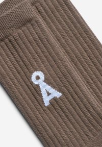 Braune, gerippte Socken aus Strickstoff mit einem deutlich sichtbaren weißen Logo. Das Design betont die Textur und den Farbkontrast.