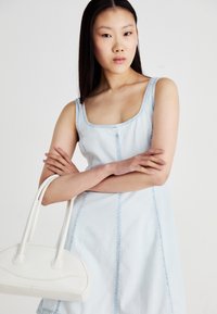 Light blue denim dress with a square neckline and contrasting seams, paired with a small white handbag featuring a rounded shape and two handles.