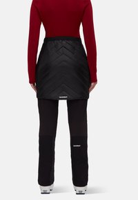 Black insulated skirt with chevron pattern, worn over black pants. Red long-sleeve top, featuring sleek design. Brand logo visible.
