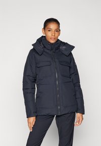 Marineblå pufferjakke med glidelås, doble frontlommer og justerbar hette. Har et strukturert stoff og et varmt, isolert design.