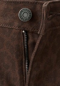 Los pantalones de algodón marrón cuentan con una bragueta con cremallera y un botón negro circular con la inscripción "MNG DESIGN DENMARK" en relieve. Presentan un patrón de espiga texturizado.