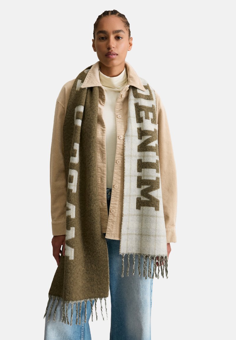 Sjaal van een wolblend met olijfgroene en lichtgrijze ruitpatronen, met franjes aan de randen en gedurfde letters waarop "DENIM" staat.