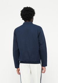 Chaqueta azul marino con cuello, cinturilla elástica y mangas largas; tejido suave con un diseño limpio y minimalista.